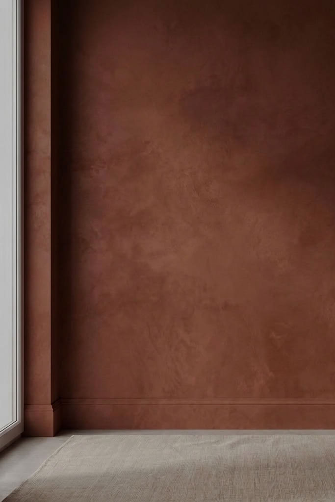 A textured, warm terracotta-brown wall with a distressed finish, shown in a minimalist interior setting with a light-colored floor and a window frame on the left.