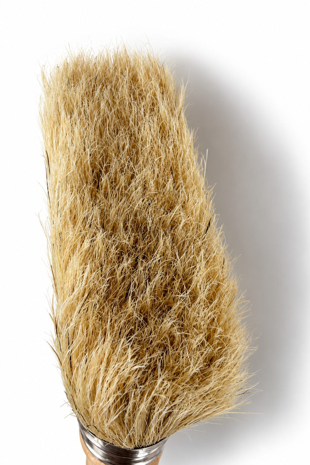 A close-up of a natural fiber hairbrush with dense golden-brown bristles and a silver metal ferrule, set against a plain white background.