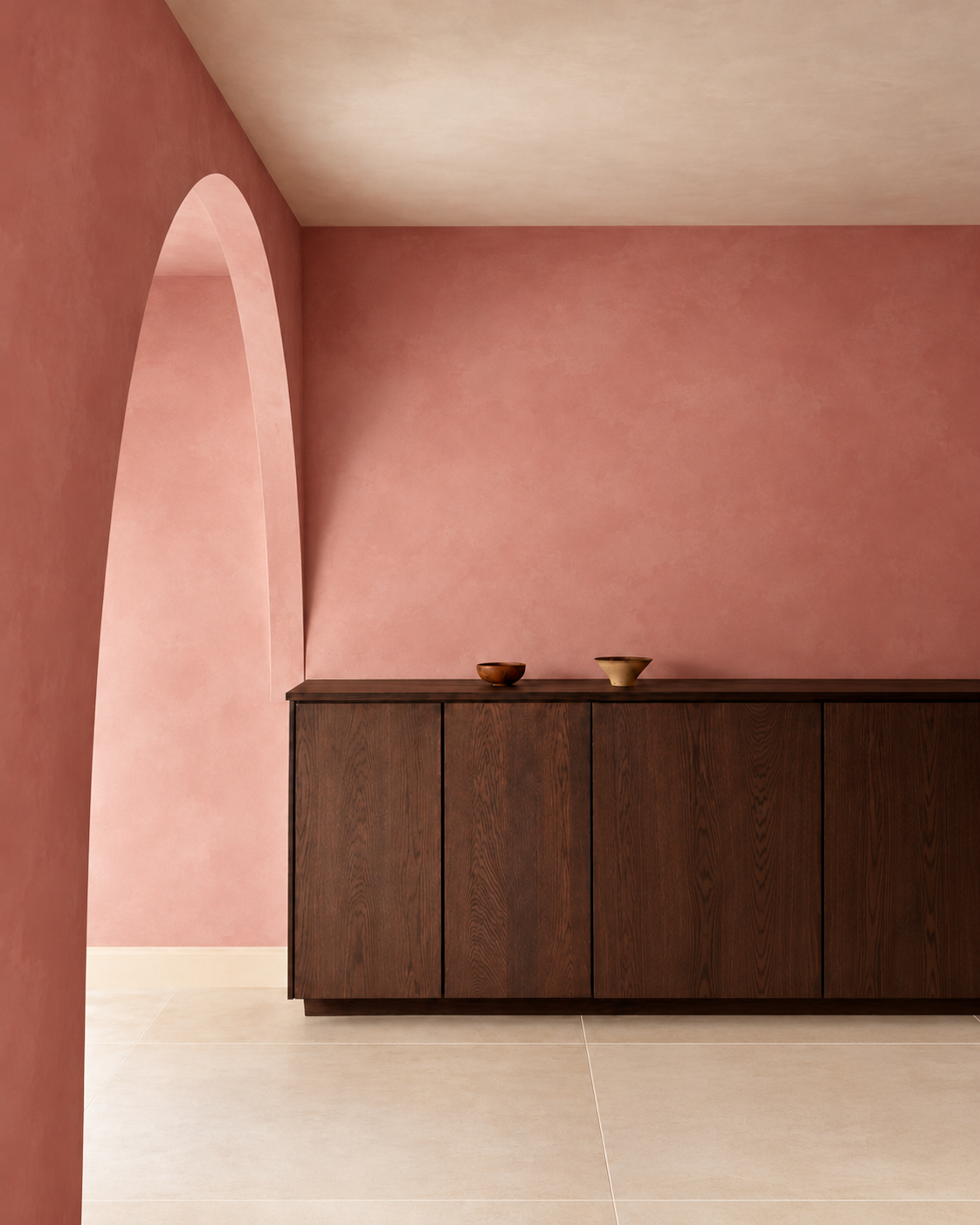 A modern dark wood sideboard cabinet in a minimalist room with a dusty rose pink wall, a matching archway on the left, and light beige tiled flooring.